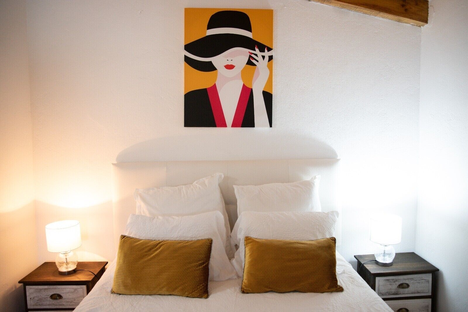 Ein Schlafzimmer mit einem Bett, zwei Nachttischen, einer Lampe auf jedem Tisch, einem Wandbild und einem Kopfteil.