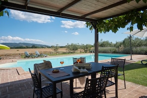 Un patio techado con una mesa y sillas, piscina y vistas al paisaje.