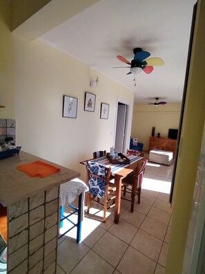 A dining area with a wooden table and chairs, a kitchen counter, and a ceiling fan. - Apartment in pine forest with sea view. Located in the natural park of Porto selvaggio (Nardò)