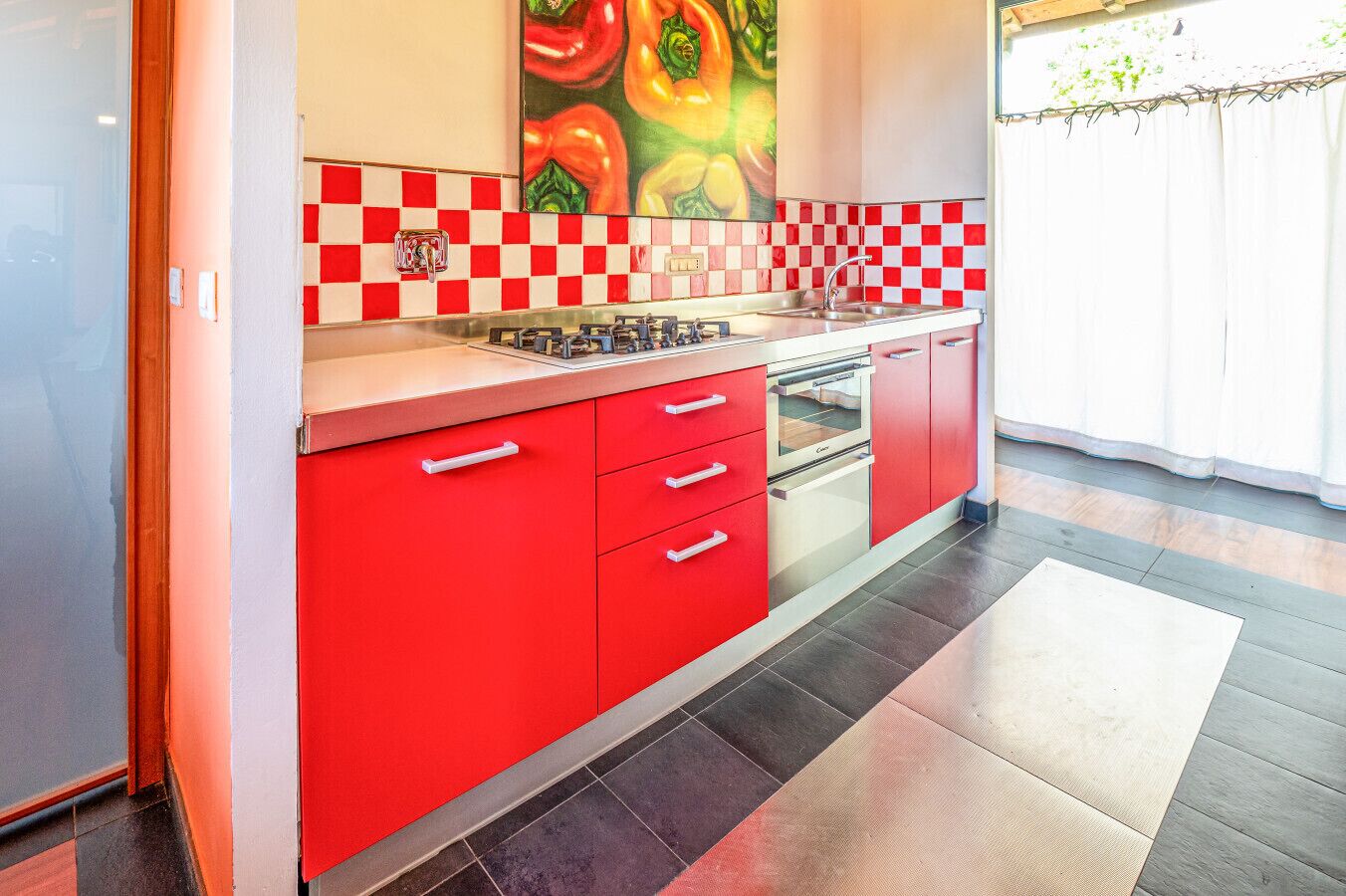 Une cuisine avec des meubles de couleur rouge, un dosseret à carreaux et une grande fenêtre offrant une belle vue.