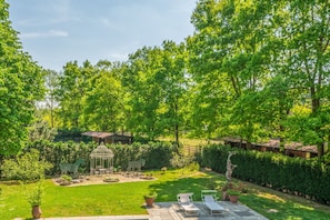 Ein üppiger Garten mit einem Laubenrondell, einer Sitzgelegenheit und einem kleinen Teich.