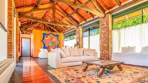 A spacious room with a high wooden ceiling, a white sofa, a patterned rug, and a colorful wall mural.