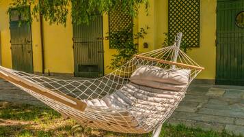 A hammock with a cushion, set against a yellow building with green shutters.