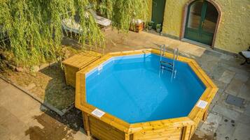 Una piscina de madera octogonal con escalera, rodeada de baldosas de piedra y una cubierta de madera.