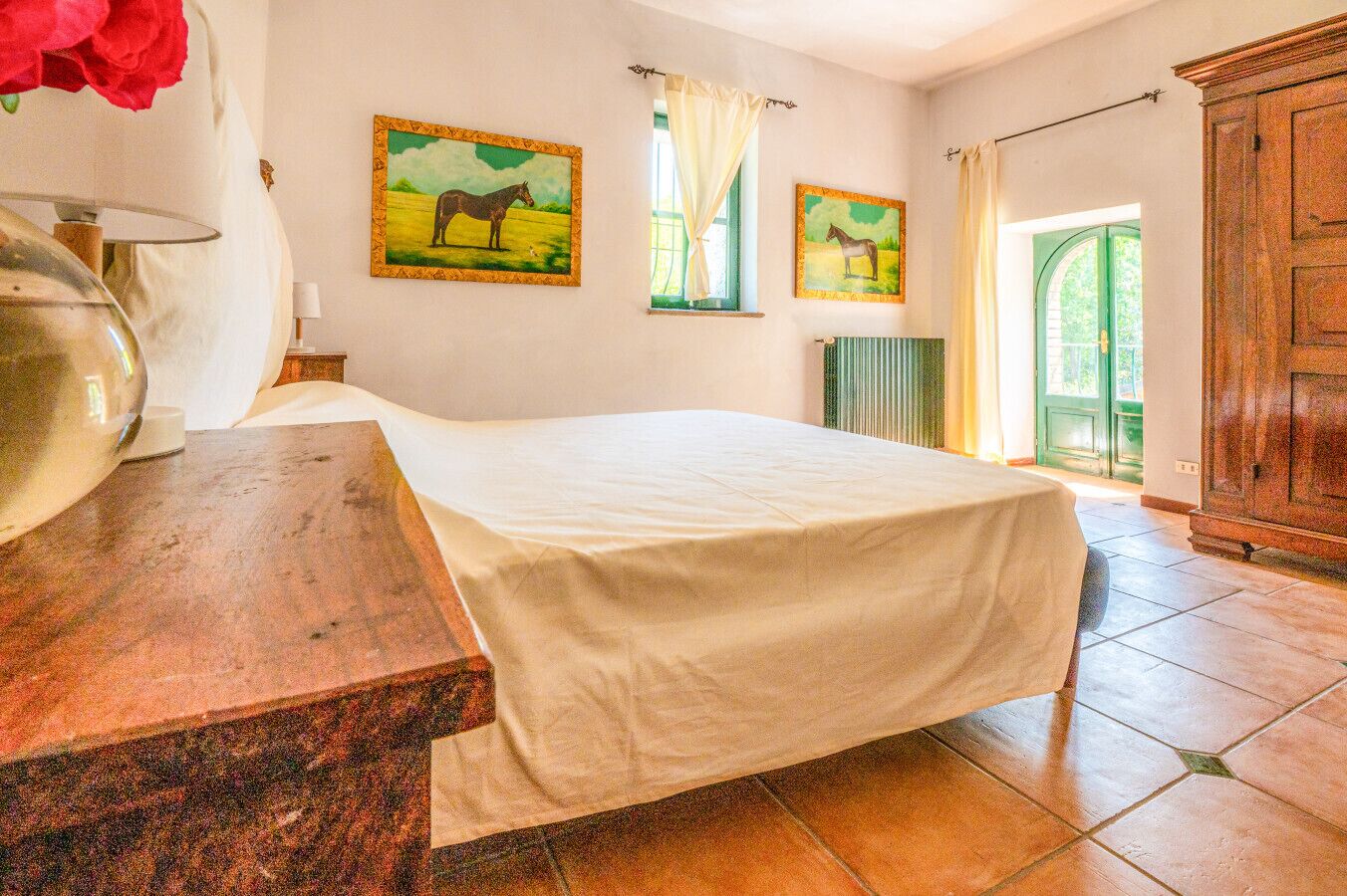 A bedroom with a bed, a wooden desk, a radiator, and two paintings of horses.