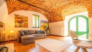 Ein Wohnzimmer mit Backstein-Decke, einem grauen Sofa, einem Glastisch und einer grünen Tür.