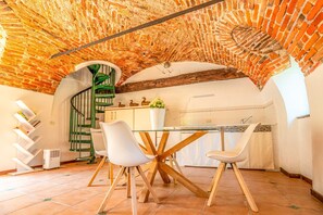 A kitchen with a brick ceiling, a spiral staircase, white chairs, and a glass table. - Cristal Apartments - Green Apartment (Masserano)