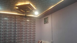 A bedroom with a patterned wall, a bed, and a ceiling light fixture. - Yashoda Kunj (Mathura)