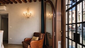 A corner room with a leather armchair, a chandelier, and a large window with a view of buildings and water. - Viola Suite Luxury Canal View Central Venice (Venezia)