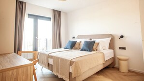 A bedroom with a bed, a chair, a bedside table, and a window with curtains. - Villa Orkula Rab with Heated Pool, Gym & Sea View (Rab)