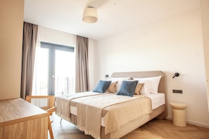 A bedroom with a bed, a chair, a bedside table, and a window with curtains.