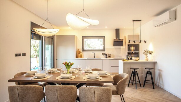 A modern kitchen with a dining area, featuring a large island, pendant lighting, and a view of the outdoors. - Villa Orkula Rab with Heated Pool, Gym & Sea View (Rab)