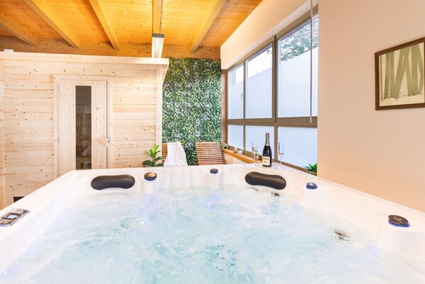 A spa room with a hot tub, wooden walls, and a large window.