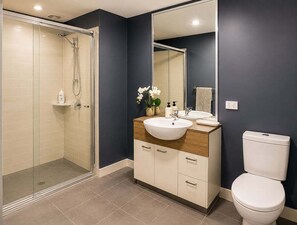 Et moderne badeværelse med en glasbrusekabine, et træbord med vask og et toilet.