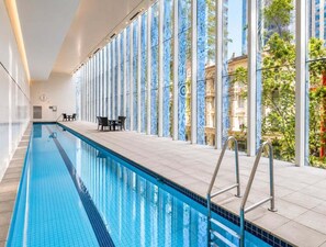 An indoor swimming pool with clear glass walls, a tiled floor, and a view of buildings outside. - Stylish Brisbane City 1BR Apartment Retreat (Brisbane)