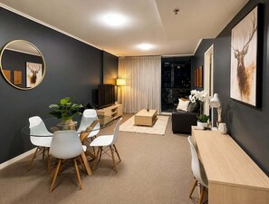 A modern living room with a round mirror, a glass dining table with chairs, a sofa, a TV, and artwork on the walls. - Stylish Brisbane City 1BR Apartment Retreat (Brisbane)