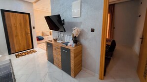 A modern room with a wooden cabinet, a flat-screen TV, a vase with flowers, and a bed with a beige headboard.