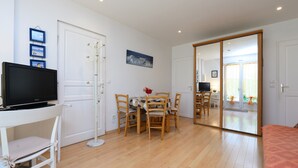 A room with a TV on a stand, a dining table with chairs, a large mirror, and a bed. - Holiday Home 'Ty Lydian' with Private Terrace, Private Garden and Wi-Fi (Arradon)