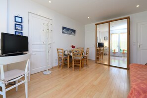 A room with a TV on a stand, a dining table with chairs, a large mirror, and a bed. - Holiday Home 'Ty Lydian' with Private Terrace, Private Garden and Wi-Fi (Arradon)