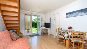 A modern living room with a sofa, a dining table with chairs, a TV, and a staircase. - Holiday Home 'Ty Lydian' with Private Terrace, Private Garden and Wi-Fi (Arradon)