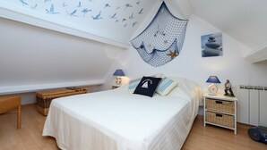 A bedroom with a bed, two nightstands, a wicker bench, and a wall decoration. - Holiday Home 'Ty Lydian' with Private Terrace, Private Garden and Wi-Fi (Arradon)