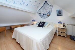 A bedroom with a bed, two nightstands, a wicker bench, and a wall decoration. - Holiday Home 'Ty Lydian' with Private Terrace, Private Garden and Wi-Fi (Arradon)