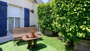 Un banco de madera, una mesa con una planta en maceta y un seto verde en un jardín.