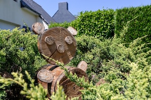 A wooden sculpture resembling a bear in a garden with dense foliage and a house in the background. - Guest Room 'Couette Et Café' with Shared Garden and Wi-Fi (Arradon)