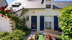 Una casa de dos pisos con puerta principal, un balcón pequeño y un jardín con flores y plantas.