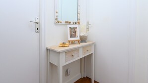 Un tocador blanco con espejo, un cuadro enmarco y conchas decorativas.
