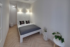 Een moderne slaapkamer met een bed, nachtlampjes, een klein rond tafeltje met een plant en een witte muur met een structuur.