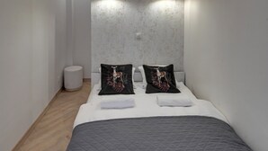 Hotellihuone, jossa on sänky, kaksi seinään kiinnitettyä valaisinta, pyöreä roskakori ja kuvioitu seinä.