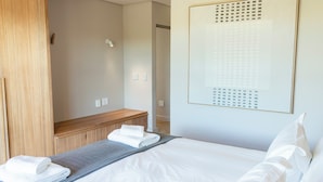 Hotellihuone, jossa on sänky, puinen penkki, seinään kiinnitetty valaisin ja kehystetty taideteos.