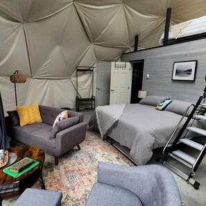 Eine Zelthütte mit Bett, Stuhl, kleinem Tisch und einer Leiter.