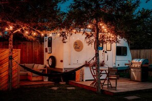 Un véhicule récréatif à l’extérieur blanc, portant une enseigne « The Nook », équipé d’un barbecue et d’un hamac.