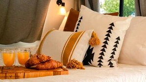 Una cama con almohadas, una mesita de noche con croissants y jugo de naranja, y una ventana con cortinas.