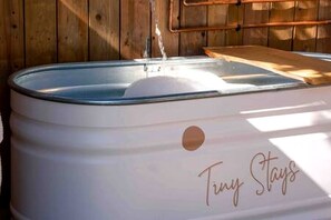 Una fontaneta blanca amb forma de bótes i un petit orifici per a sortida d'aigua, amb la inscripció 'Tiny Stays', en un entorn de fusta.