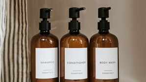 Tres botellas de champú, acondicionador y jabón de cuerpo sobre una superficie blanca.