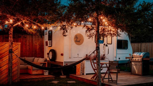 Una caravana recreativa con exterior blanco, un letrero que dice 'The Nook', una parrilla y una hamaca.