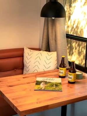 A wooden table with a magazine, two bottles, and a black lamp in a room with a window and a brown leather couch.