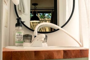 A bathroom with a white sink, a round mirror, a bottle of hand soap, and a towel hanging on the wall.