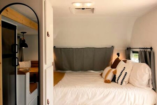 Une chambre à coucher avec un lit, une fenêtre avec des rideaux, une porte et un miroir.