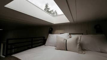 Un dormitorio con tragaluces, una cama con almohadas, una mesita de noche y un aparador.