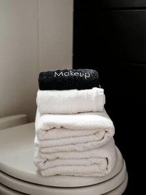 Gestapelte, gefaltete Handtücher auf einem weißen Toilettendeckel.