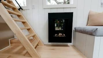 A room with a wooden staircase, a fireplace, a sofa, and a window.