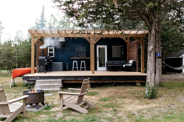 A wooden deck with a grill, outdoor seating, and a covered area with a door.