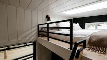 Una cama litera con cabecera, una ventana y una manta en el suelo.