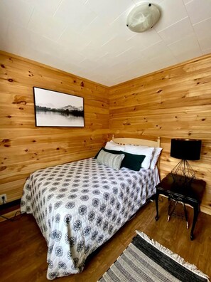 Une pièce aménagée comme un chalet en bois, avec un lit, un téléviseur fixé au mur et une image d’un lac accrochée au mur.