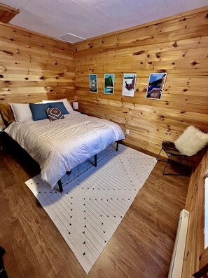 A wooden-paneled room with a bed, a chair, and wall art. - Picturesque Cottage with Spacious Large Backyard and BBQ in Canada (Brigus South)