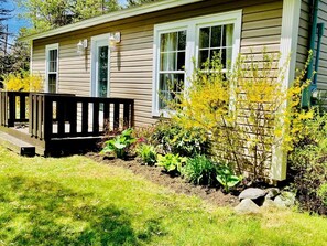 A house with a deck, a garden with various plants, and a window with a curtain. - Picturesque Cottage with Spacious Large Backyard and BBQ in Canada (Brigus South)